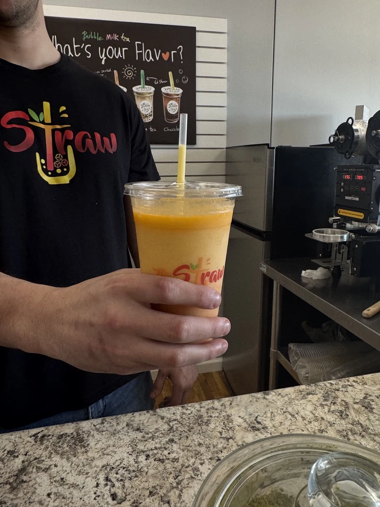 A Straw team member serving a freshly made orange smoothie at the counter